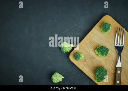 Placer broccoli verdi segmenti da un piccolo cucchiaio. Mangiare sano pattern su sfondo scuro. Spazio Copia vista dall'alto. Cibo vegetariano. Foto Stock