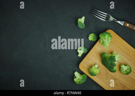 Placer broccoli verdi segmenti da un piccolo cucchiaio. Mangiare sano pattern su sfondo scuro. Spazio Copia vista dall'alto. Cibo vegetariano. Foto Stock