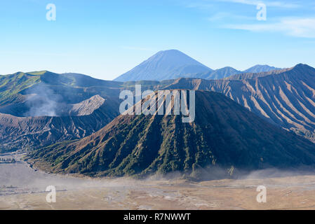 Il monte vulcano Bromo cratere erutta nella caldera, dietro il Gunung Batok, con Gunung Semeru in background, Java, Indonesia. Foto Stock