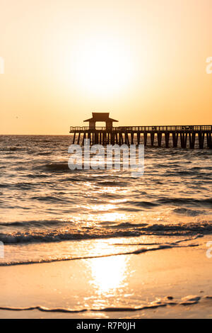 Naples, Florida giallo e arancione tramonto nel golfo del Messico con il tramonto dal Molo Jetty di legno, con trend con orizzonte di riferimento e la sagoma scura onde dell'oceano, sunlig Foto Stock