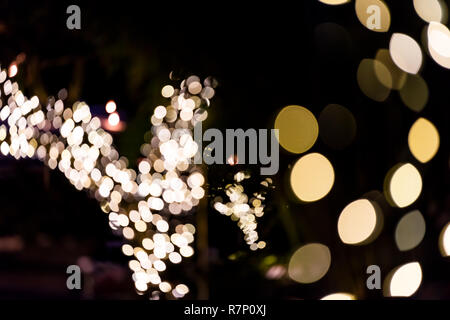 Vacanze di Natale bokeh sfondo astratto con cerchi oro accese le luci di decorazione su Palm tree di notte sera nero scuro Foto Stock