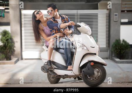 Felice giovane coppia romantica indossando occhiali da sole seduto su uno scooter. Foto Stock