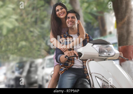 Felice giovane donna mentre tiene il suo partner da dietro mentre è seduto su uno scooter. Foto Stock