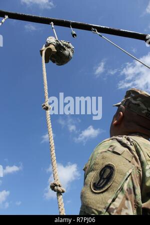 Esercito personale di riserva Sgt. Jonathan Davis con il 104th Training Division (LT) raggiunge la parte superiore della corda ostacolo mentre un 95th Training Division (entrata iniziale formazione) sicurezza sottufficiale guarda su durante la formazione 108th comando (IET) guerriero migliore concorrenza a Camp Bullis, Texas, Marzo 19-24, 2017. Foto Stock