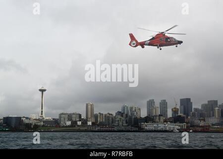 Un MH-65 Delfino elicottero dalla guardia costiera Stazione aria Port Angeles vola attraverso la skyline di Seattle Mar. 29, 2017. L'elicottero è stato nell'area di Seattle mentre il guardacoste Munro era tirando in porta per la Munro la cerimonia di messa in servizio il sabato. Stati Uniti Coast Guard Foto Stock