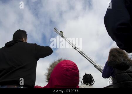 512Th Airlift Wing familiari guarda un fire fighter con il 436th ingegnere civile Squadron salire una scala firetruck su Dover Air Force Base, Del., 1 aprile 2017. I membri della famiglia hanno partecipato ad un mese del bambino militare che coinvolgesse guidate di una C-5M Super Galaxy, C-17 Globemaster III, la stazione dei vigili del fuoco e una dimostrazione di lavoro militare cani. Foto Stock