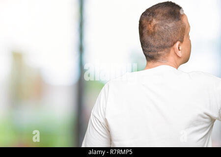 La mezza età uomo arabo wearig t-shirt bianco su sfondo isolato in posa rivolta indietro dietro con il dito mano Foto Stock