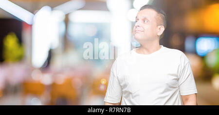 La mezza età uomo arabo wearig t-shirt bianco su sfondo isolato sorridente cercando lato e lo sguardo lontano pensando. Foto Stock