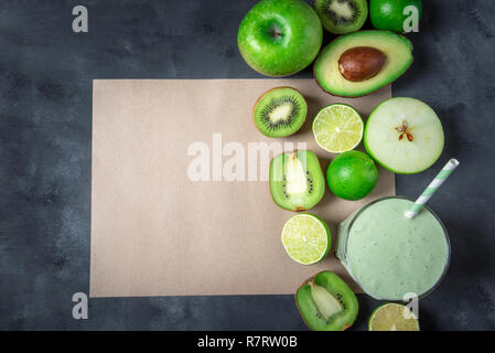 Frutti di verde e di un vetro con un smoothie, su un vuoto di carta marrone della pagina su un sfondo grigiastro. Detox drink. Contesto di dieta. Mangiare sano. Foto Stock