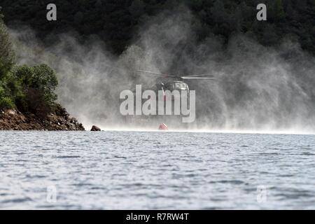 Un UH-60 Black Hawk dalla protezione nazionale della California è appena visibile come si scende a 600 gallone Bambi Bucket nel serbatoio Pardee in iun, California, 8 Aprile durante il 2017 Wildland formazione antincendio. California aria Guardia attivi erano la formazione con CAL FIRE air operations come un preludio alla prossima stagione di fuoco. Foto Stock