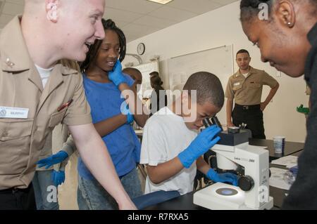 Portsmouth, Va. (7 aprile 2017) un quarto grado studente alla vista parco Scuola Elementare guarda attraverso il microscopio in corrispondenza della stazione di laboratorio mentre Hospital Corpsman 3rd Class Michael Murphy (sinistra) spiega ciò che lo studente sta vedendo. Più di una dozzina di membri del personale da al Centro Medico Navale di Portsmouth ha partecipato in Career Day presso la scuola elementare di Portsmouth impostando tre interattivo di scienza, tecnologia e Ingegneria matematica (gambo)-stazioni connesse alla scuola di scienza lab. Foto Stock