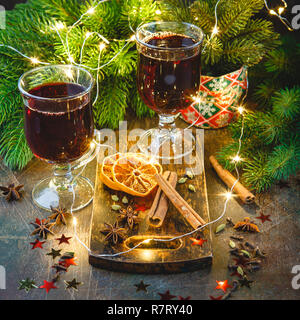 Le coppe di vetro di vin brulé con spezie e arancio secco di pezzi sul tagliere di legno su sfondo scuro. Tradizionale bevanda di Natale Foto Stock