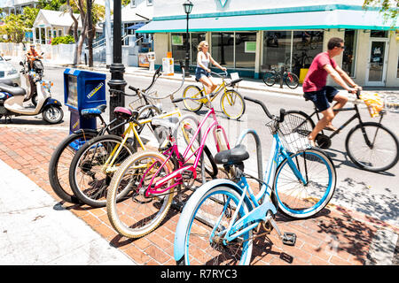 Key West, Stati Uniti d'America - 1 Maggio 2018: gente giovane equitazione biciclette in Florida City travel, giornata di sole sulla strada, parcheggiato rack, biciclette, news stand Foto Stock