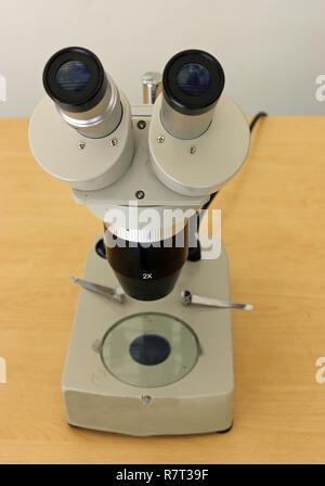 Microscopio binoculare con supporto utilizzato per il college di insegnamento o il lavoro di laboratorio su un marrone chiaro tavolo. Foto Stock