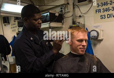 Oceano atlantico (Mar. 31, 2017) della Cmdr. Stephen W. Aldridge, comandante della guidato-missile destroyer USS Mason (DDG 87), riceve un taglio di capelli da navi militari della prima classe Quintin Ellis. Mason, parte di Eisenhower Carrier Strike gruppo, è in corso la partecipazione in un esercizio di supporto a sostegno della flotta ottimizzato il piano di risposta (OFRP). Foto Stock