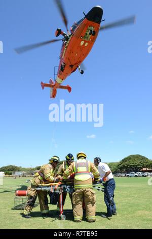 Un MH-65 Delfino elicottero equipaggio dalla guardia costiera Stazione aria Barbieri dal punto di Oahu, conduce una evacuazione medica di dimostrazione con membri provenienti da Maui County Fire Department come parte di un evento D.A.R.E. per Kualapuu carta pubblica la scuola dei bambini a Kaunakakai Ball Park, Molokai, Aprile 7, 2016. Il rally si è tenuta a informare i bambini sui pericoli della droga e comprendeva anche dimostrazioni da parte della guardia costiera Stazione aria Barbieri punto, Guardia nazionale, Maui il dipartimento di polizia della contea di Maui Vigili del Fuoco, Hawaii Dipartimento della Terra e delle risorse naturali e numerose altre agenzie. Foto Stock