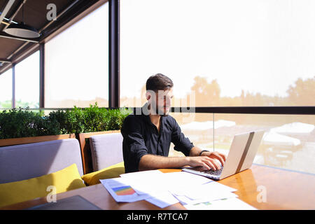 Lavoratore di ufficio ordinamento di carte sul tavolo vicino al computer portatile. Foto Stock