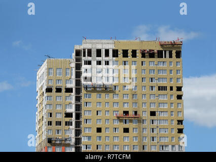 Processo di montaggio di isolamento su appartamento edificio sulla facciata incompiuta moderna casa urbana oltre il cielo blu con nuvole vista verticale Foto Stock