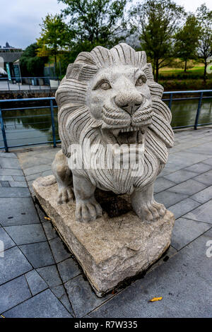 Cina leone di pietra scultura con la bocca aperta e il fiume alberi sullo sfondo Foto Stock