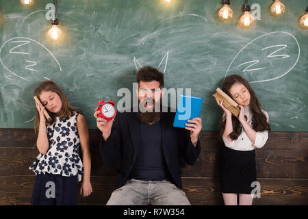 Insegnante e le ragazze gli studenti in aula, lavagna su sfondo. Bambini e insegnanti con disegnato da chalk corna. Uomo con barba urlando mentre studentesse fanno finta di dormire. Terribile lezione concetto. Foto Stock