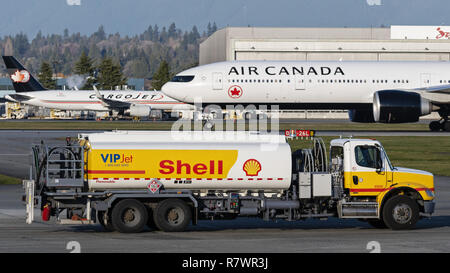 Richmond, British Columbia, Canada. 6 dicembre, 2018. Un guscio del combustibile per aviazione carrello procede lungo la pista di atterraggio all'Aeroporto Internazionale di Vancouver. Sullo sfondo un Air Canada Boeing 777-300ER prende-off. Credito: Bayne Stanley/ZUMA filo/Alamy Live News Foto Stock