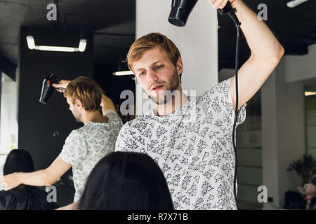 Professional sorridente stilista maschio soffiare l'asciugatura donna capelli con un essiccatore in salone Foto Stock