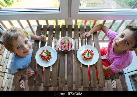 Due ragazzi di mangiare per colazione viennese di cialde con gelato e fragole Foto Stock