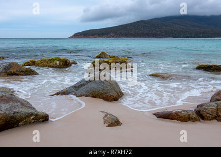 Spiaggia a Wineglass Bay, Parco Nazionale di Freycinet, Tasmania con rocce in primo piano e il blu del mare in un giorno nuvoloso Foto Stock