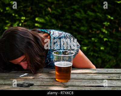 Una donna sbuffare una linea di cocaina su un tavolo di legno con un bicchiere di birra sul lato Foto Stock