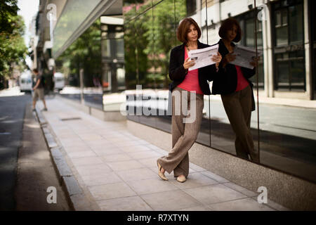 Vista laterale di una donna elegante leggendo un giornale. Foto Stock