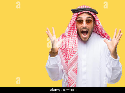 Giovane uomo bello indossare keffiyeh su sfondo isolato celebrando crazy e sorpreso per il successo con le braccia sollevate e aprire gli occhi urlando eccitato Foto Stock