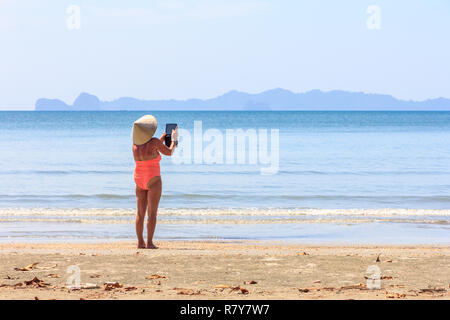 Donna prendendo foto su Ipad su Chang Lang beach, Trang, Thailandia Foto Stock