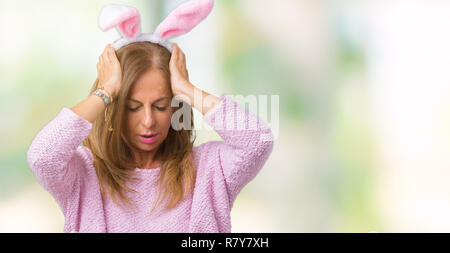 La mezza età brunette donna che indossa la pasqua orecchie di coniglio su sfondo isolato che soffrono di mal di testa disperato e ha sottolineato perché il dolore ed emicrania Foto Stock