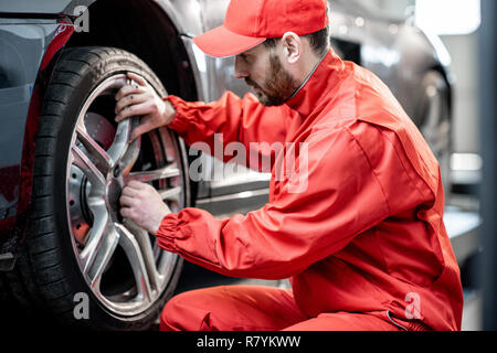 Auto di servizio lavoratore in rosso uniforme di sostituzione della ruota di una vettura sportiva al pneumatico servizio di montaggio Foto Stock