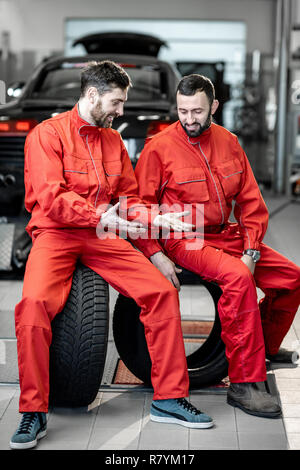 Servizio auto di lavoratori in rosso uniforme avente una pausa seduti insieme sulle ruote al pneumatico servizio di montaggio Foto Stock