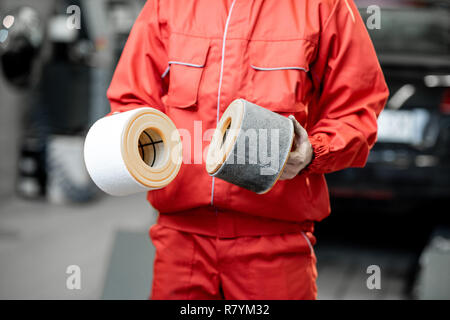 Meccanico automatico in rosso uniforme tenendo premuto di nuovo e usato il filtro dell'aria permanente al servizio di auto, vista da vicino con nessun volto Foto Stock
