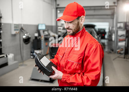 Ritratto di un bel meccanico automatico in rosso uniforme del vaso di contenimento con olio motore in corrispondenza del servizio auto al seguito Foto Stock