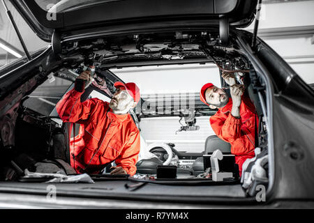 Due auto service lavoratori in rosso uniforme di smontaggio nuova auto interno apportando alcuni miglioramenti interni Foto Stock