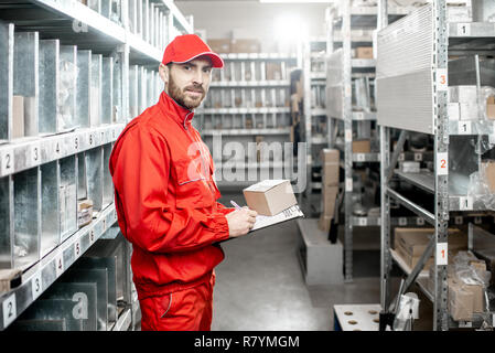 Ritratto di un lavoratore di magazzino in rosso uniforme riempimento alcuni documenti di controllo merci presso il deposito Foto Stock