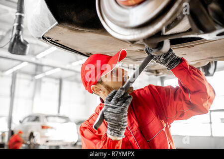 Meccanico automatico in rosso uniforme auto diagnosi sul paranco all'auto di servizio Foto Stock