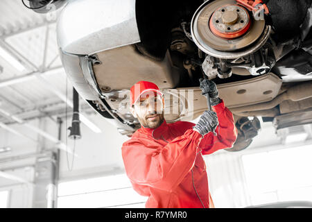 Meccanico automatico in rosso uniforme auto diagnosi sul paranco all'auto di servizio Foto Stock