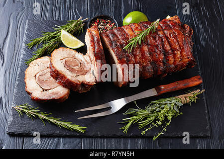 Vista aerea di fettine di maiale arrosto involtino - Porchetta, deliziosa carne di maiale arrosto di culinaria italiana tradizione vacanze su un vassoio di ardesia con rosmarino e Foto Stock