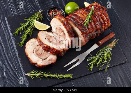 Vista aerea di fettine di maiale arrosto involtino - Porchetta, deliziosa carne di maiale arrosto di culinaria italiana tradizione vacanze su un vassoio di ardesia con rosmarino e Foto Stock