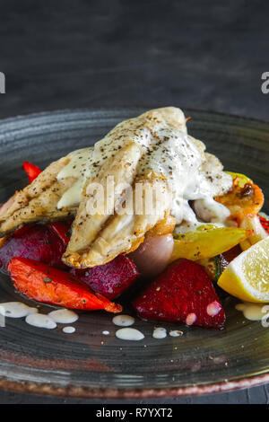 Pesce fritto di filetto con grigliate di barbabietole, carote, peperone, zucchine, aglio su sfondo scuro Foto Stock