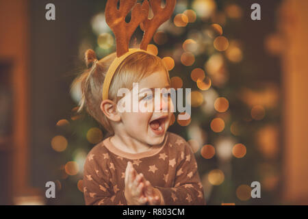 Bambino su kid's Christmas party, carino piccolo bambino in costume rudolphs battendo le mani e godendo di matinée con piacere che trascorrono le vacanze vicino a albero di Natale Foto Stock