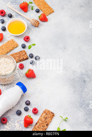 Cereali organici granola bar con bacche con cucchiaio di miele e un vasetto di avena e bottiglia di latte da bere su sfondo di pietra. Vista dall'alto. Fragola, Lampone Foto Stock