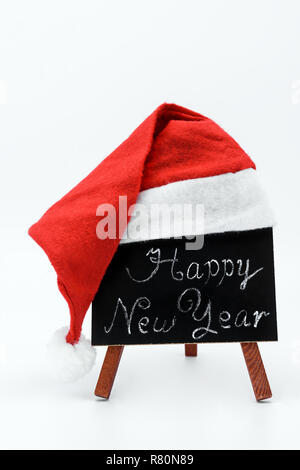 Una lavagna con il testo "Felice Anno Nuovo", scritto in gesso rivestito con un berretto di Babbo Natale su un isolato sullo sfondo bianco. Foto Stock