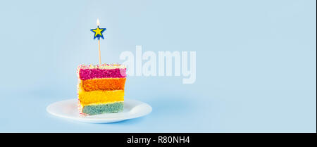 Fetta di torta arcobaleno con birning candela a forma di stella sul bianco piastra rotonda isolata su sfondo blu. Happy bithday, concetto di partito. Ampia ba Foto Stock