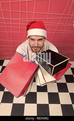 L'uomo santa tenere i sacchetti in bianco e nero del pavimento a scacchi. Shopper in Red Hat con paperbags, vista dall'alto. Natale e Anno Nuovo presenta. Inverno vendita, il concetto di shopping. Vacanze a preparazione e celebrazione. Foto Stock