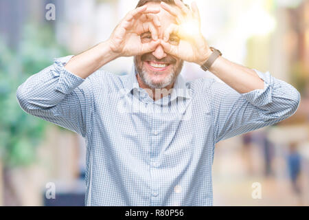 La mezza età annoso senior business man su sfondo isolata facendo ok gesto come binocolo con la lingua fuori, gli occhi guardando attraverso le dita. Craz Foto Stock